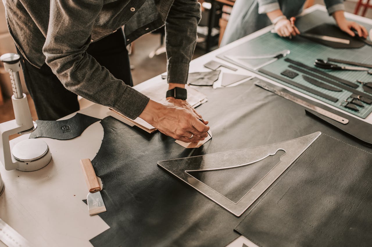 Detailed view of hands crafting leather goods with precision in a workshop setting, highlighting craftsmanship.