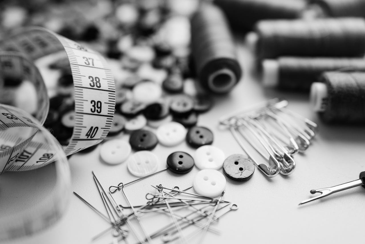 Black and white sewing materials including buttons, needles, and thread spools on a white surface.