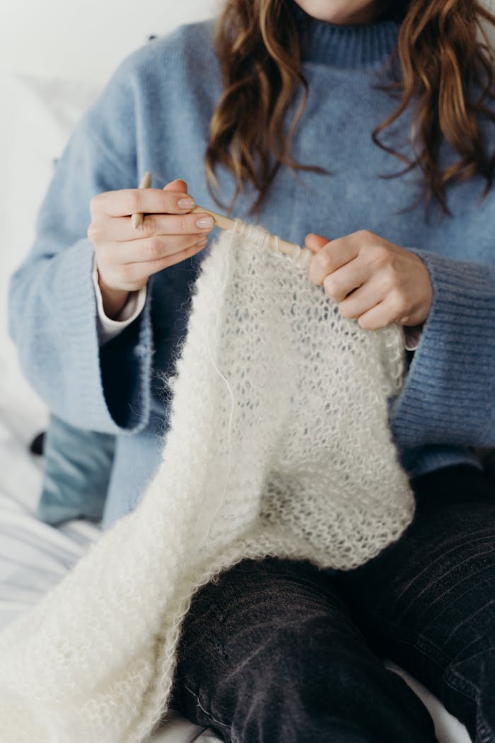 Close-up of a woman knitting with white yarn, creating a cozy winter scarf.
